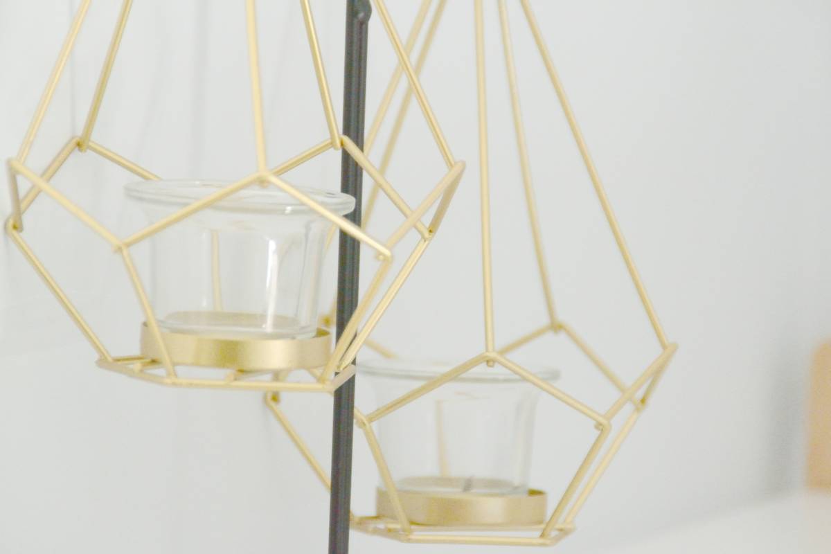 Close-up of hands arranging a gold-tone decorative ring for candles around a white pillar candle on a marble surface, showcasing texture contrast and scale